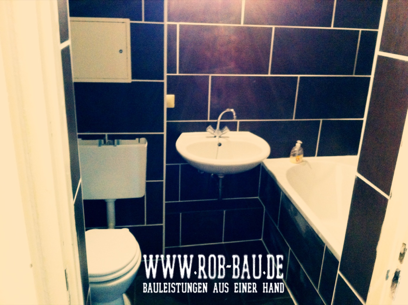 Modernisiertes Bad mit Waschbecken, WC und dunklen Fliesen